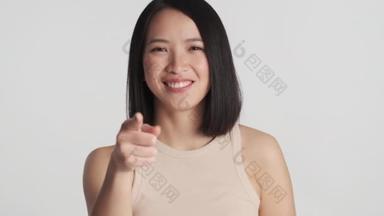 漂亮的年轻亚洲女人用食指直勾勾地对着相机，用白色的背景保持着大拇指的隔离。就像你的表情